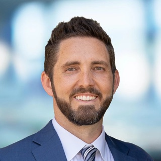 Headshot of Dr. Matt Goodwin, smiling, in a navy suit and striped tie, against a blurred blue background.